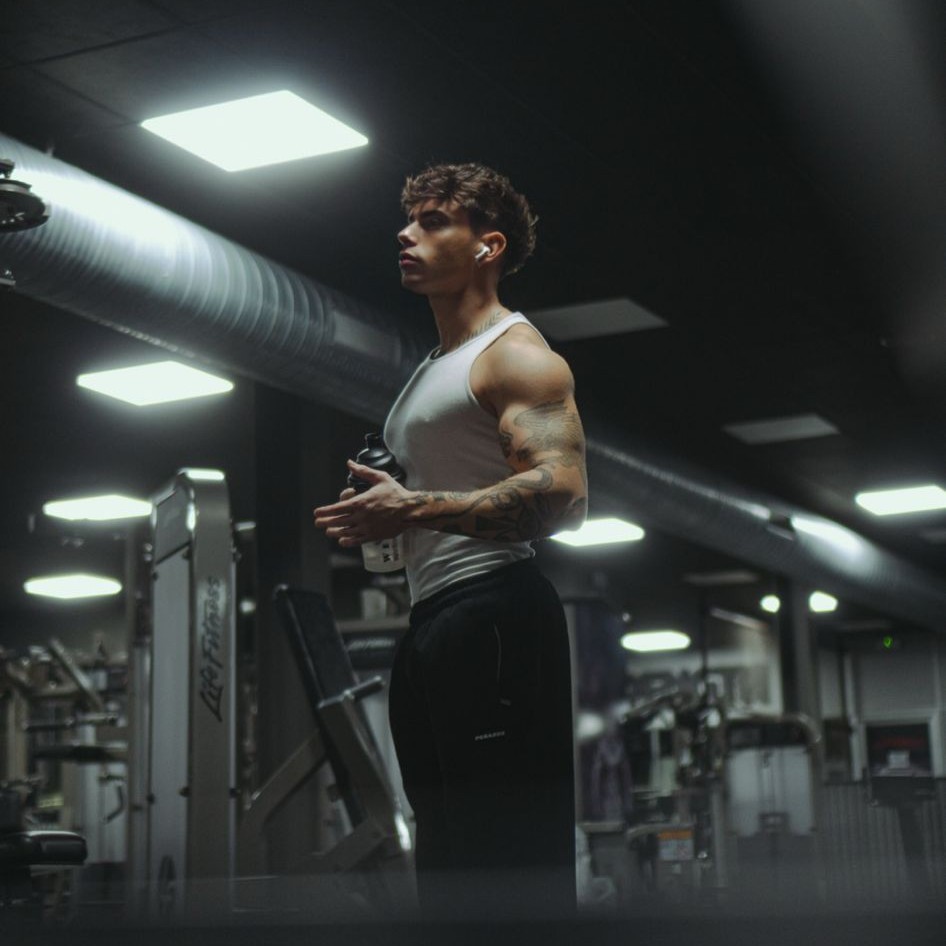Francesco Sisko Consales in palestra con canotta bianca e shaker in mano, illuminazione notturna cinematografica